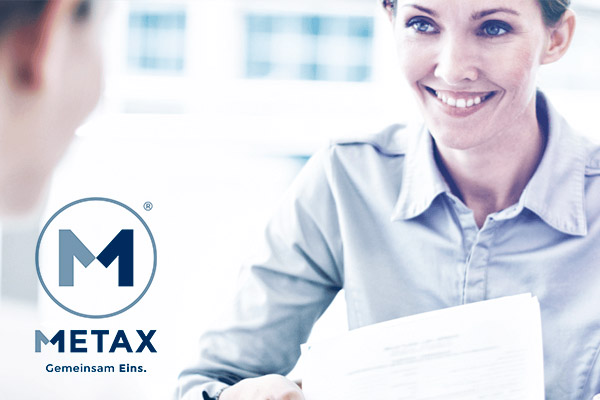 Metax - Eine Frau unterhält sich mit einem Mann an einem Schreibtisch.