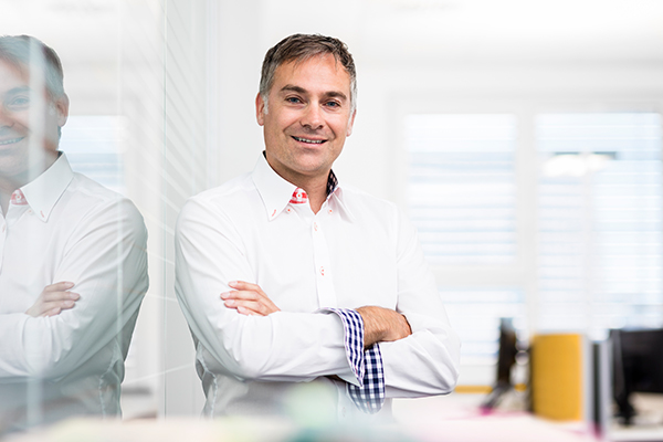 Steuerberater Stefan Reuther in einem weißen Hemd steht vor einer Glaswand in der Steuerkanzlei SWRP
